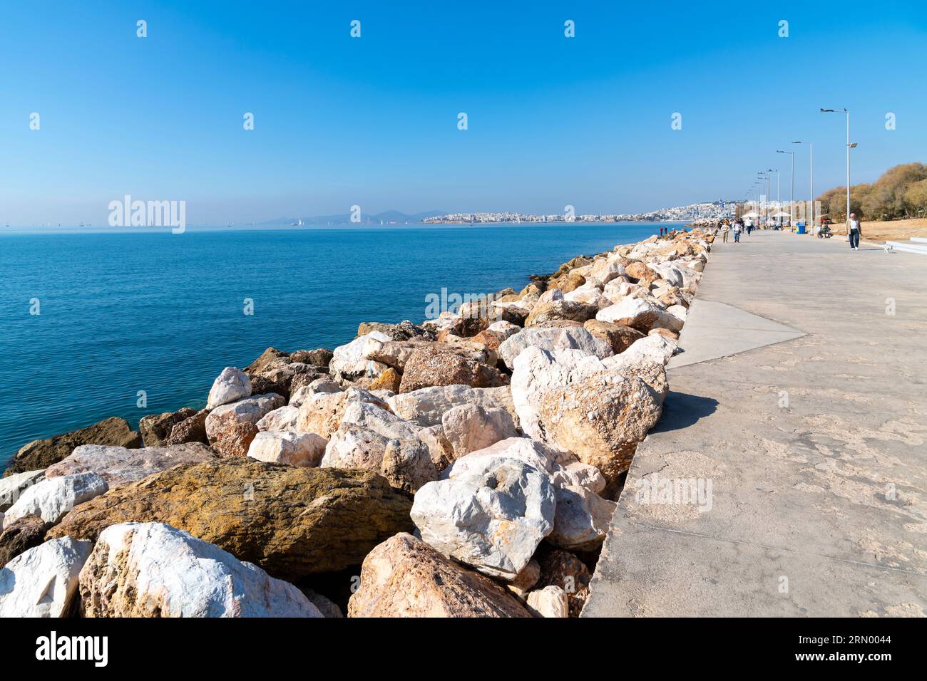 Die Fußgängerzone und Promenade am Meer entlang der Athenischen Riviera in der griechischen Stadt Palaio Faliro, mit Piräus Griechenland im Blick hinter. Stockfoto