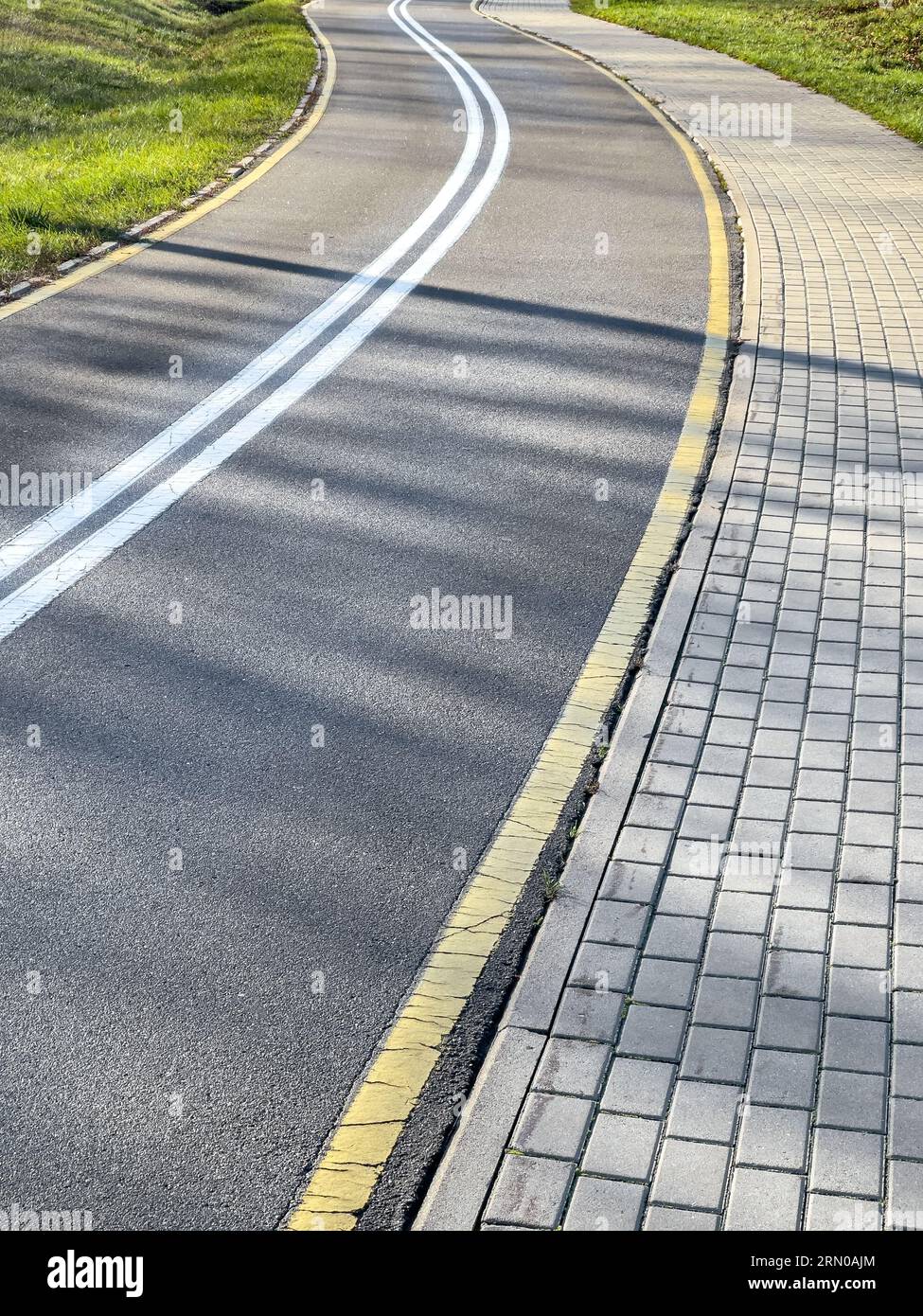 Leere, gewundene Fahrradroute im Park mit Sonnenlicht und sanften Schatten von Bäumen. Stockfoto
