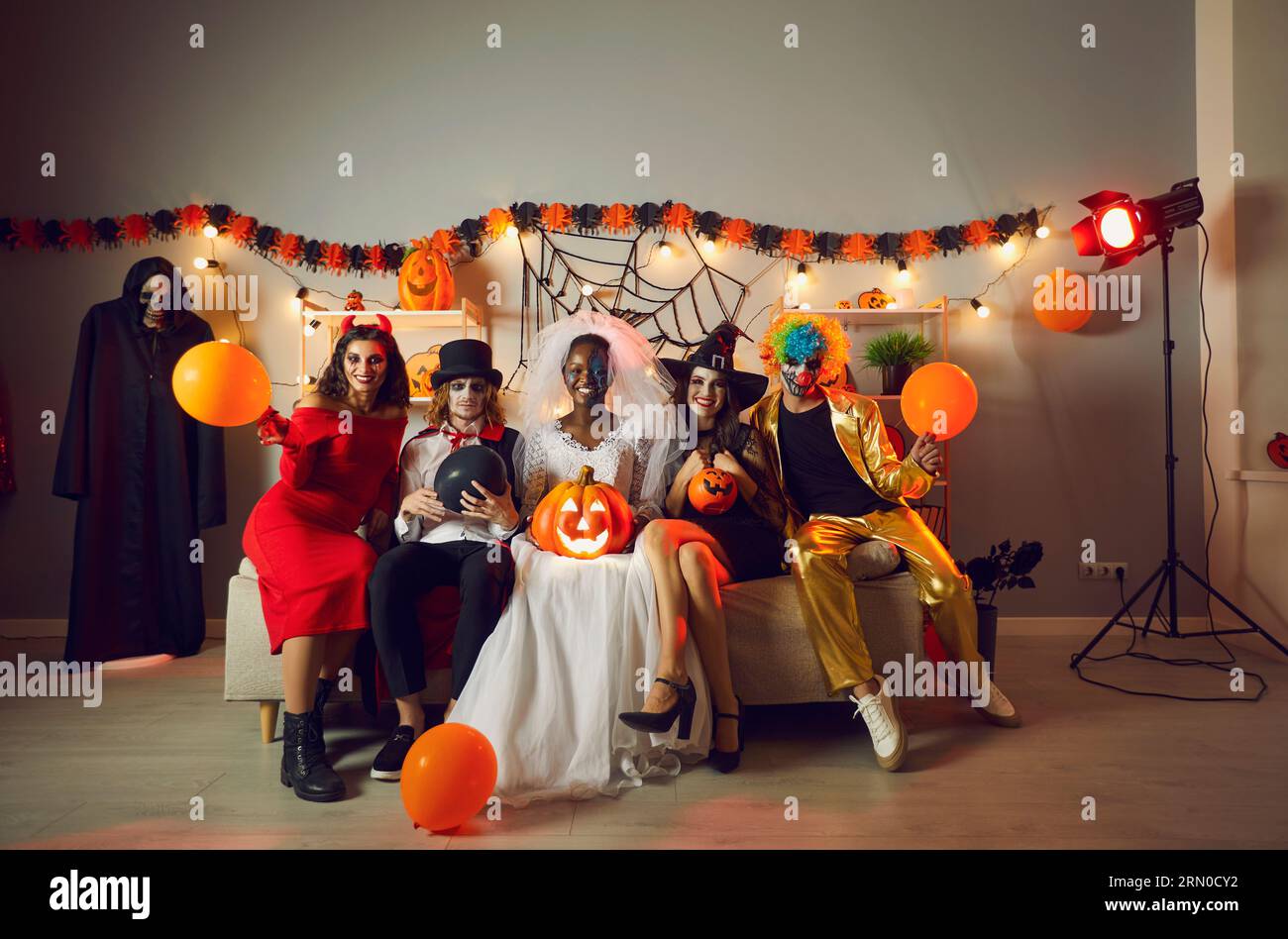 Gruppe junger Menschen in gruseligen Kostümen, die auf dem Sofa auf der Halloween-Party zu Hause sitzen Stockfoto