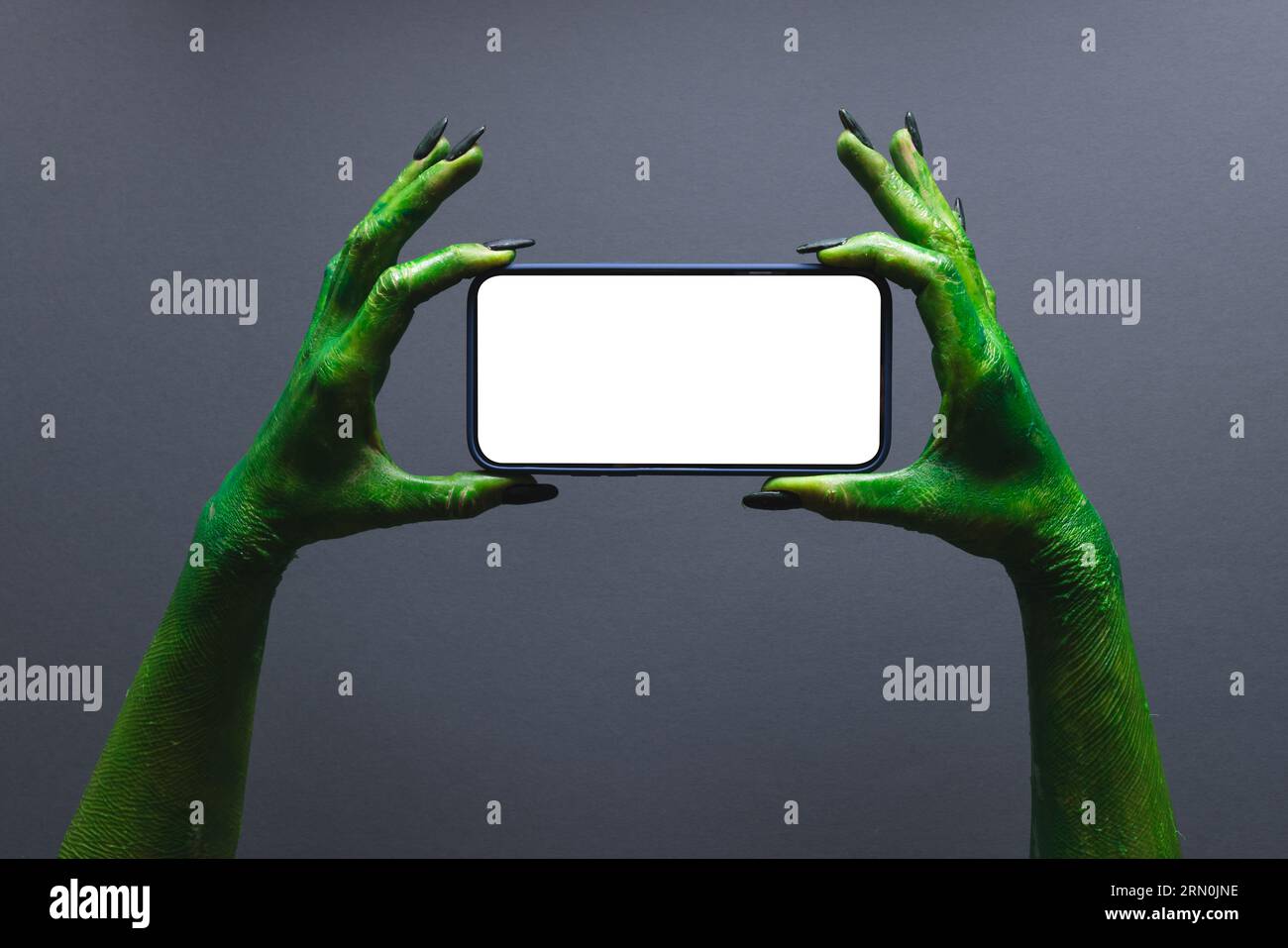 Grüne Monsterhände halten Smartphone mit Kopierraum auf grauem Hintergrund Stockfoto