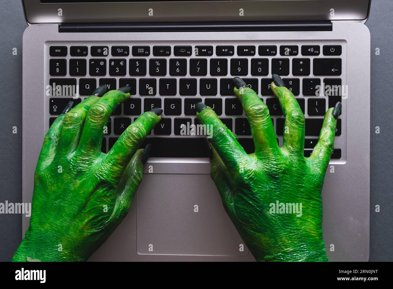 Grüne Monsterhände schreiben auf Laptop-Tastatur auf grauem Hintergrund Stockfoto