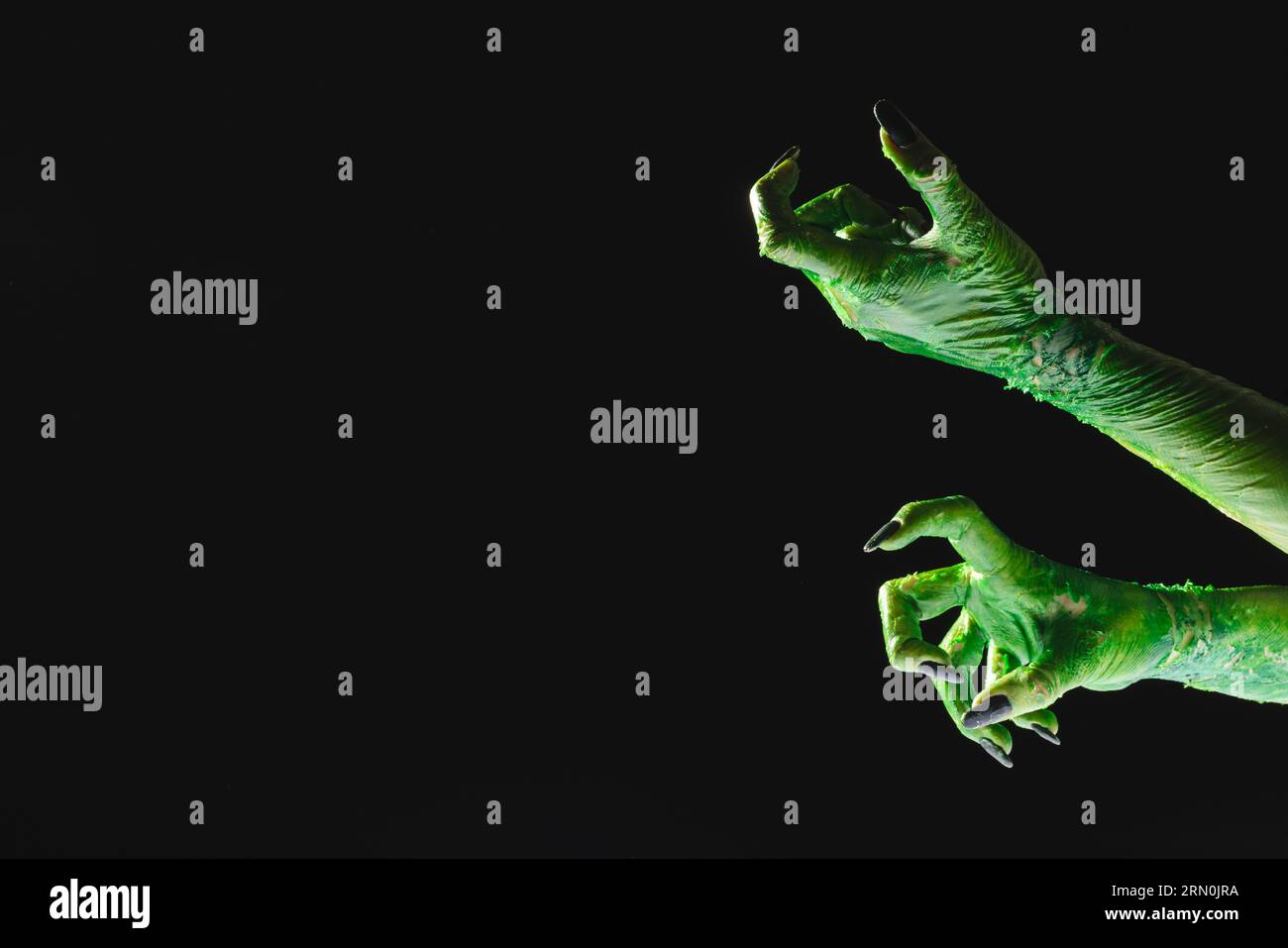 Grüne Monsterhände mit schwarzen Nägeln, die auf schwarzem Hintergrund reichen Stockfoto