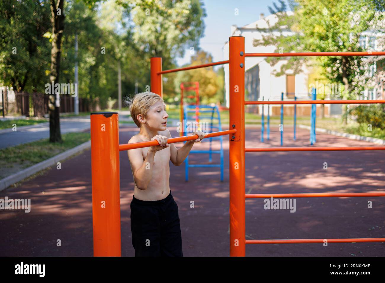 Der muskulöse Teenager streckte sein Kinn auf der horizontalen Leiste hoch. Street Workout auf einer horizontalen Bar im Schulpark. Stockfoto