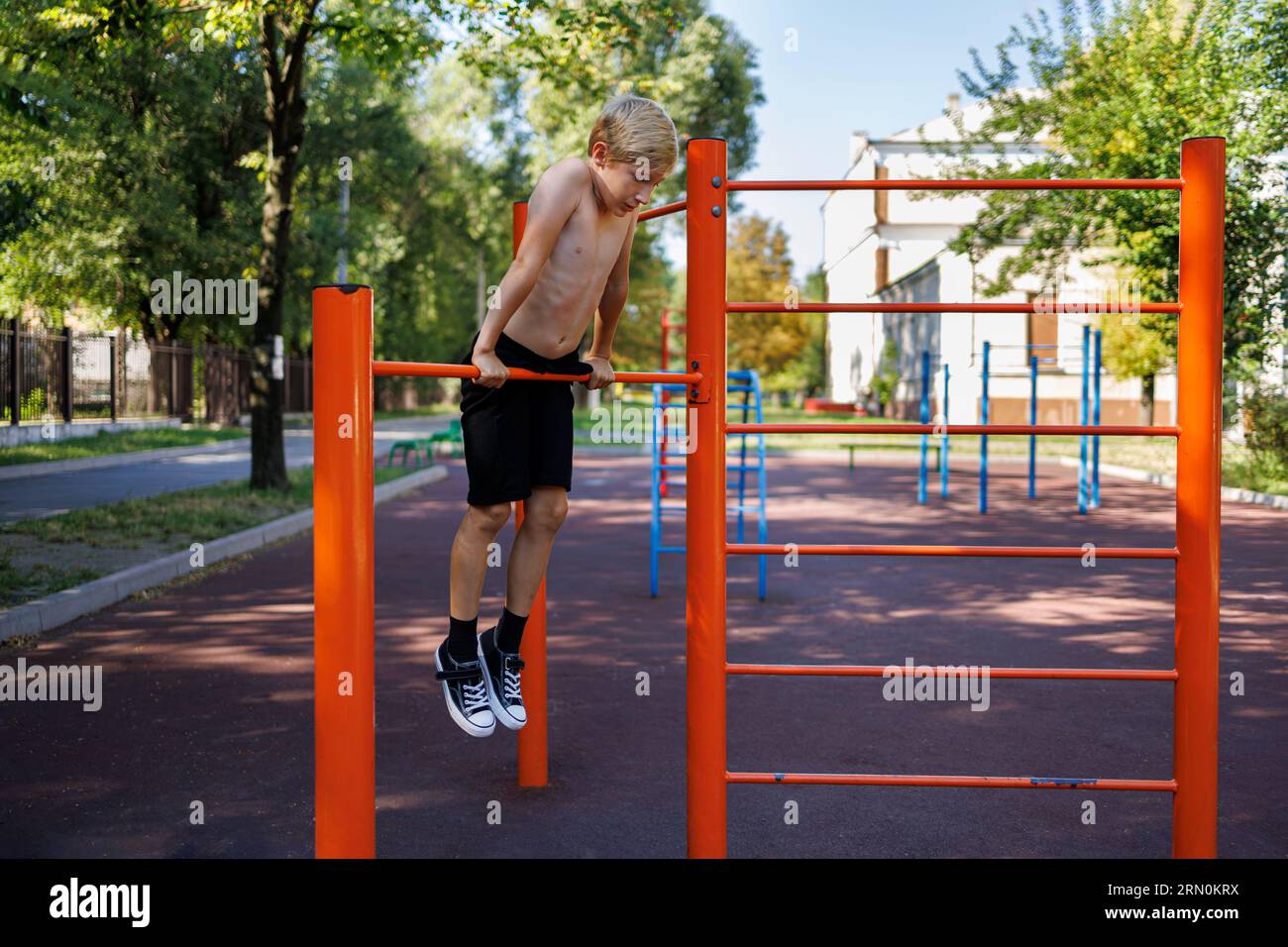 Ein Teenager-Athlet hält sich mit den Händen an die Bar und hängt daran. Street Workout auf einer horizontalen Bar im Schulpark. Stockfoto