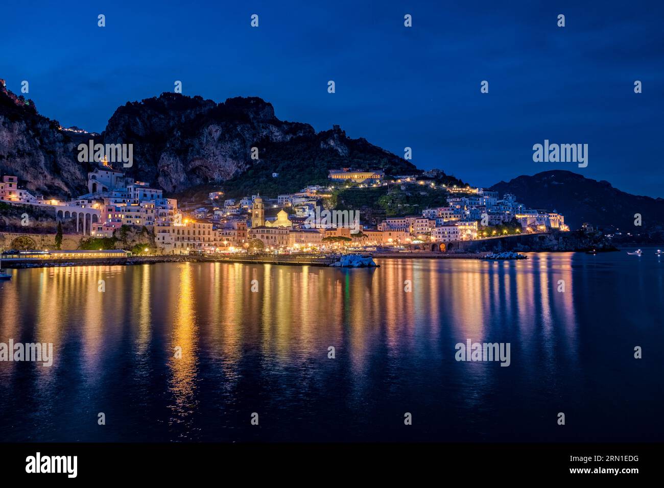 Die Häuser der Stadt Amalfi an der Amalfiküste, beleuchtet bei Nacht, reflektiert im Mittelmeer. Stockfoto