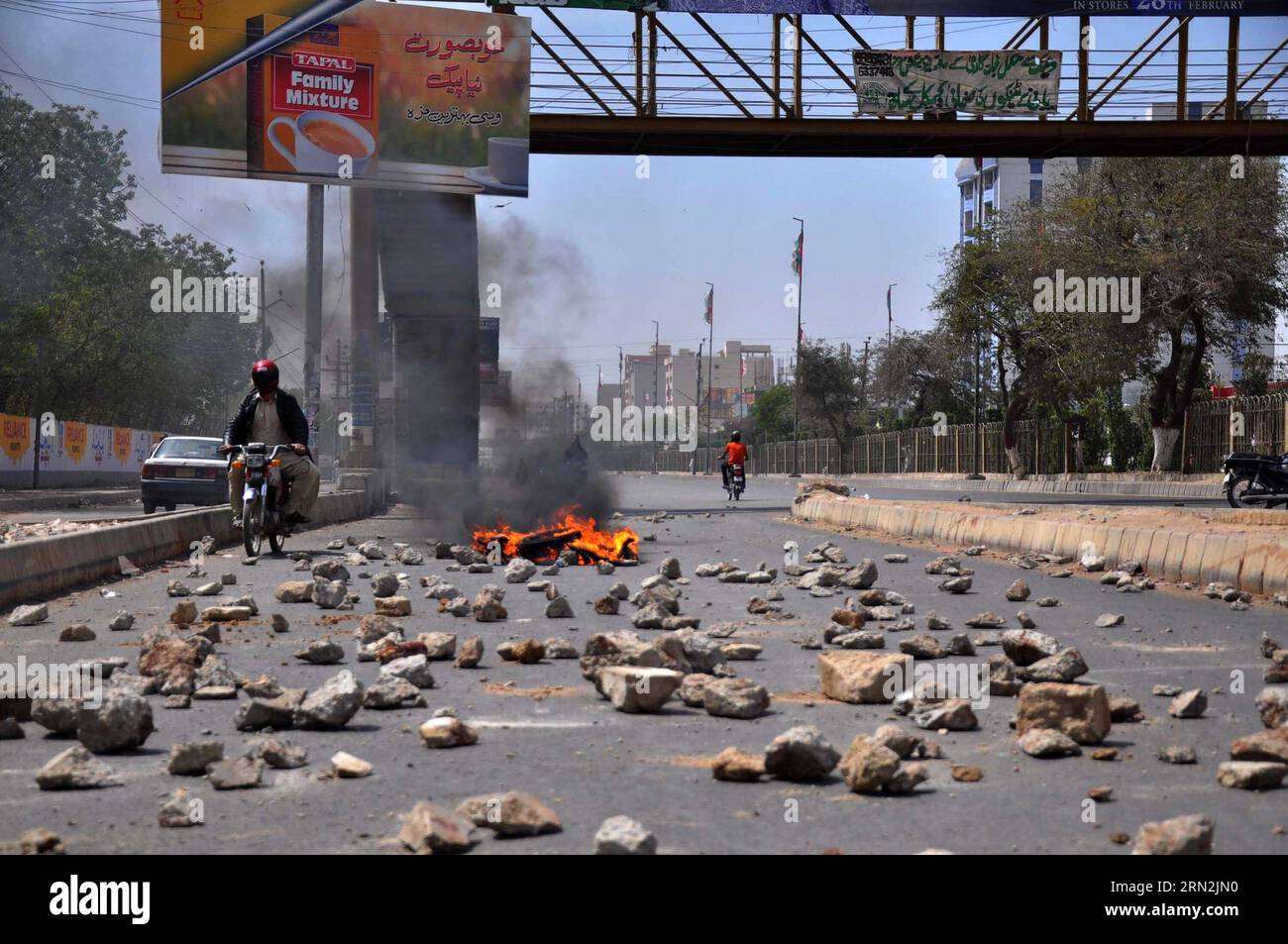 (150311) -- KARACHI, 11. März 2015 -- während eines Streiks, den die Führer der Muttahida Qaumi-Bewegung (MQM) nach einem Angriff auf das MQM-Hauptquartier in der südpakistanischen Hafenstadt Karachi am 11. März 2015 einberufen hatten, fahren Menschen an brennenden Reifen und Steinen auf einer Straße vorbei. Pakistanische paramilitärische Truppen plünderten Anfang Mittwoch das Hauptquartier einer mächtigen politischen Gruppe in der Hafenstadt Karachi und erholten Waffen und verhafteten einige Verdächtige, sagten Beamte. PAKISTAN-KARACHI-RAID Masroor PUBLICATIONxNOTxINxCHN Karachi 11. März 2015 Berühmtheiten reiten an brennenden Reifen und Steinen AUF einer Straße während eines Streiks namens Stockfoto