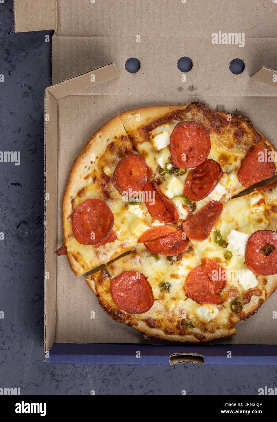 Pizza mit Feta, Chili, Käse und Peperoni - in Pizzapackverpackung Stockfoto