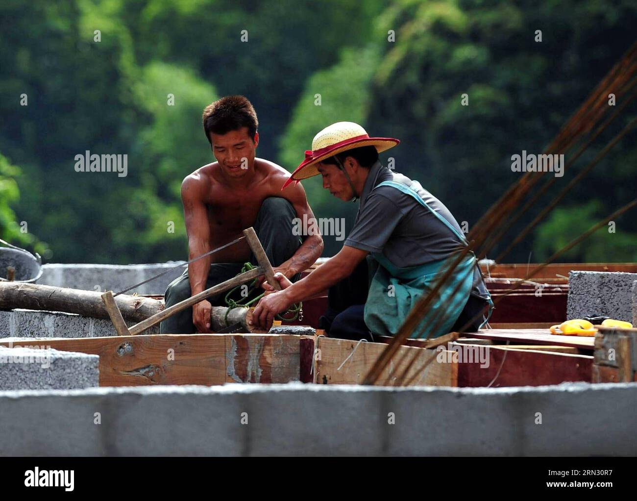 Der 33-jährige Lan Guimao (L) baut sein neues Haus in Nongyong Villge of Bansheng Township, südwestchinesische autonome Region Guangxi Zhuang, 14. Juli 2013. Wegen des Mangels an Flachland bauen die meisten Familien in den westlichen Berggebieten von Dahua ihre Häuser auf Hügeln. In den Bezirken Qibainong und Bansheng in Dahua leben Menschen der Miao-Volksgruppe seit etwa tausend Jahren in den Bergen. Sie verlassen sich auf das Pflanzen von Körnern für ihren Lebensunterhalt. Das dreistöckige Stelzengebäude ist im traditionellen Architekturstil der beiden Grafschaften gehalten. Die Menschen züchten Vieh im unteren Stockwerk, Stockfoto