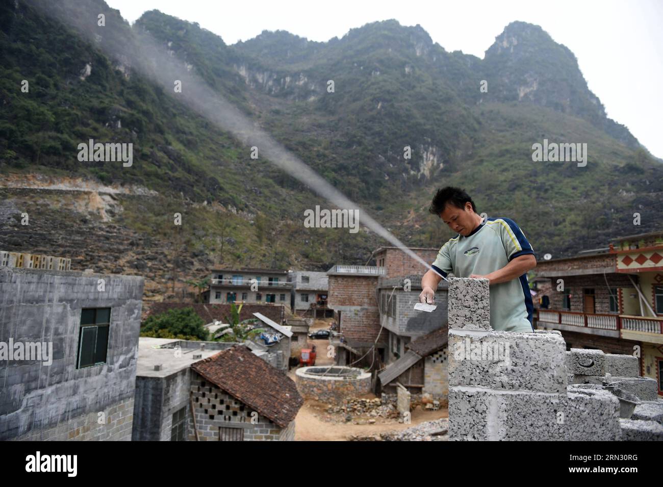 Der 40-jährige Meng Guirong baut sein neues Haus im Dorf Nongding in der Gemeinde Bansheng im südwestchinesischen Guangxi Zhuang am 28. Februar 2015. Wegen des Mangels an Flachland bauen die meisten Familien in den westlichen Berggebieten von Dahua ihre Häuser auf Hügeln. In den Bezirken Qibainong und Bansheng in Dahua leben Menschen der Miao-Volksgruppe seit etwa tausend Jahren in den Bergen. Sie verlassen sich auf das Pflanzen von Körnern für ihren Lebensunterhalt. Das dreistöckige Stelzengebäude ist im traditionellen Architekturstil der beiden Grafschaften gehalten. Menschen züchten Vieh im unteren Stockwerk, r Stockfoto