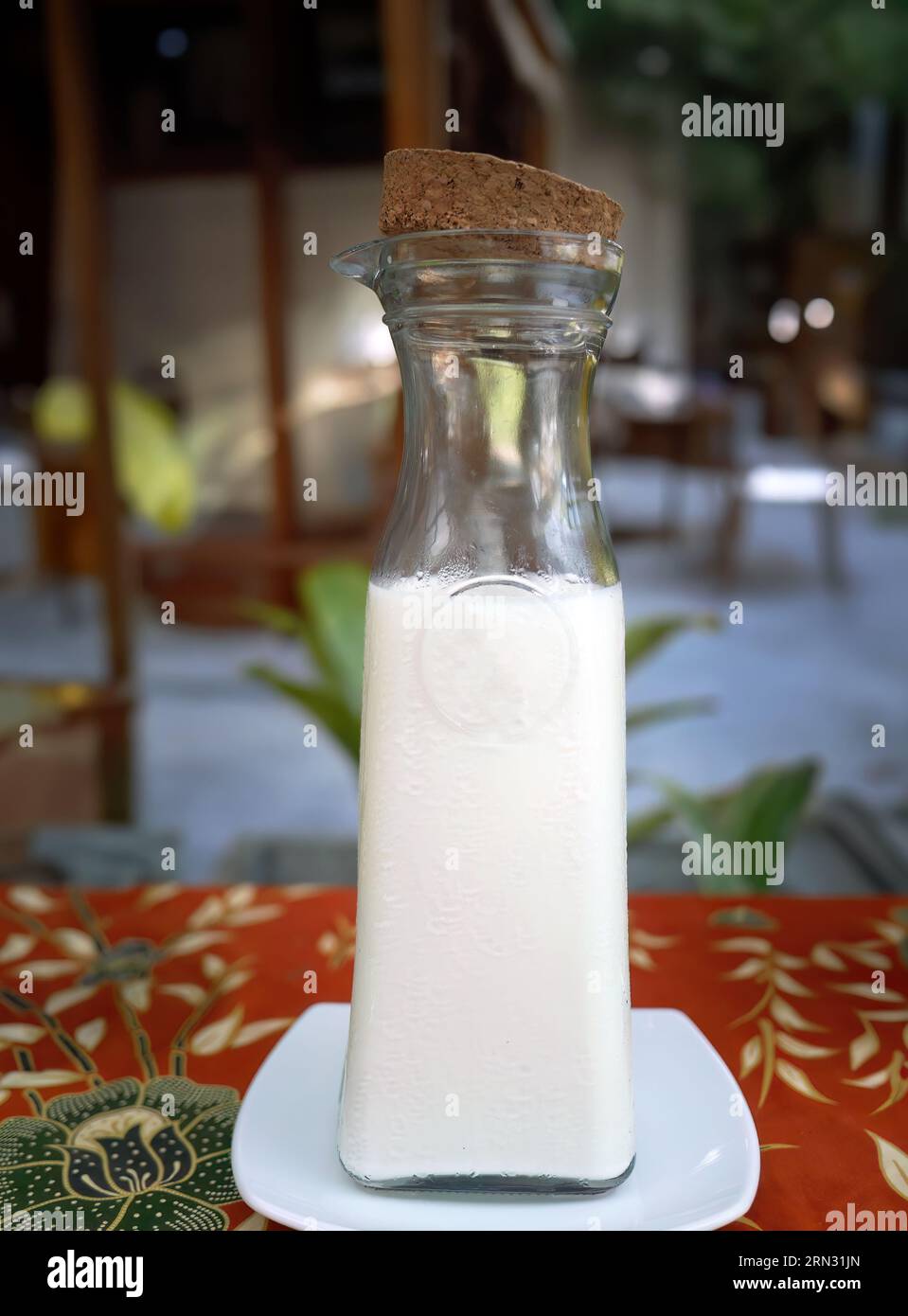 Eine Glasflasche enthielt reine Milch mit Kork, frische Getränke, Utensilien, modernes Produktdesign, Flaschendesign auf thailändischem Tischtuch mit lokalem Muster, Tradition Stockfoto