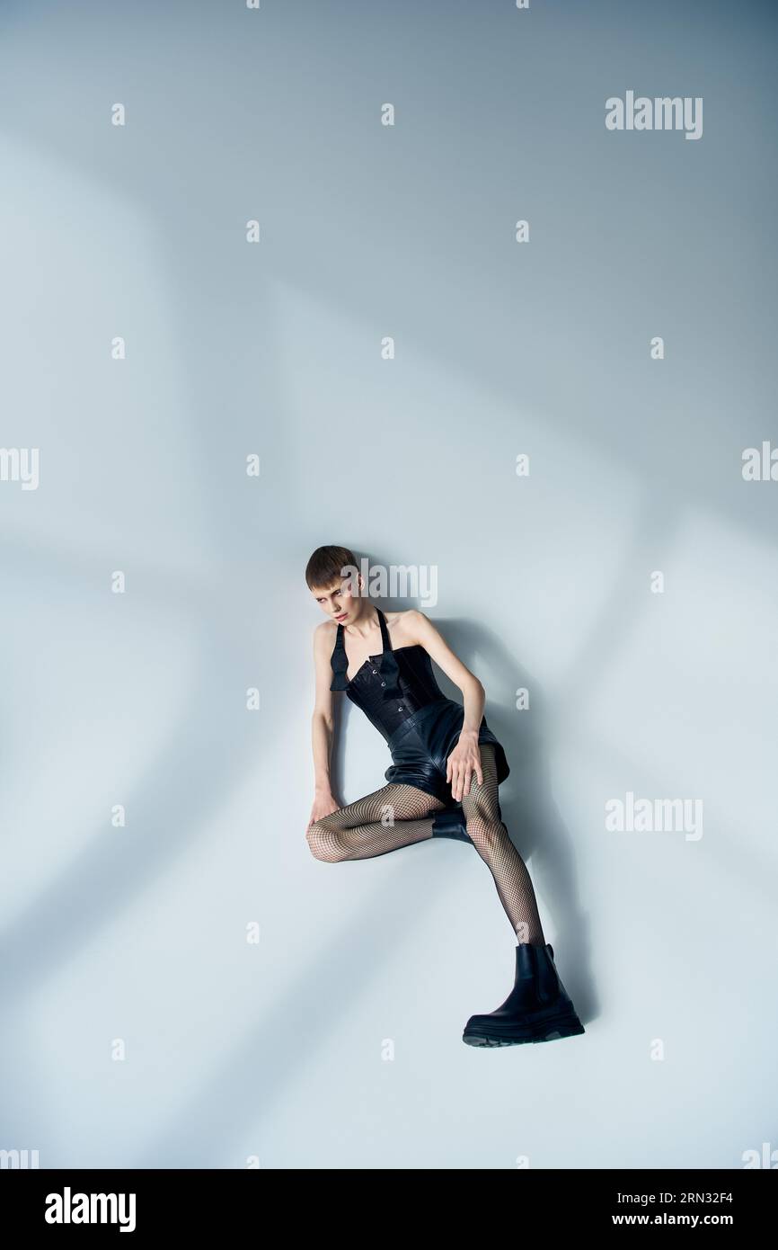 Queeres Modell in Korsett, Shorts und Stiefeln auf grauem Hintergrund, lgbt, androgyner Stil, Blick weg Stockfoto