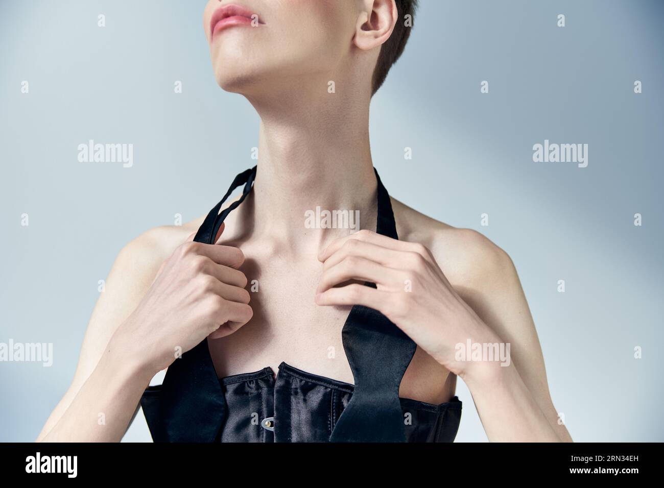 Kurzes, queeres Modell mit schminkender Krawatte am Nacken und auf grau, schön und androgyn posierend Stockfoto