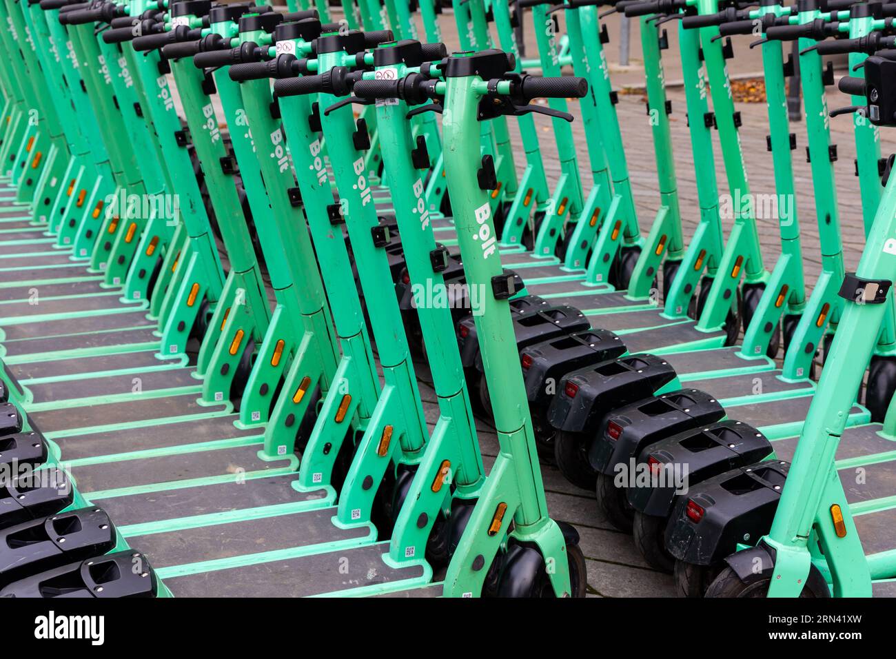 Reihen von grünen Elektrorollern, die auf einem Bürgersteig in der Stadt geparkt sind. Privatfahrzeuge für den Stadtverkehr können gemietet werden Stockfoto
