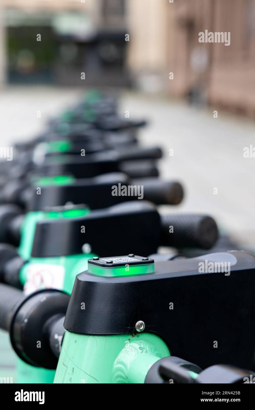 Nahaufnahme des Lenkers eines grünen Elektrorollers. Verschwommene Stadt im Hintergrund. Privatfahrzeuge für den Stadtverkehr können gemietet werden Stockfoto