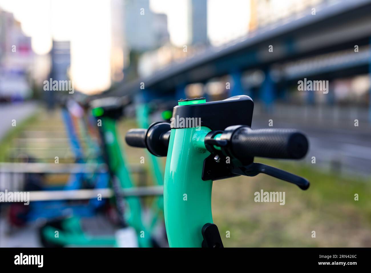 Nahaufnahme des Lenkers eines grünen Elektrorollers. Verschwommene Stadt im Hintergrund. Privatfahrzeuge für den Stadtverkehr können gemietet werden Stockfoto