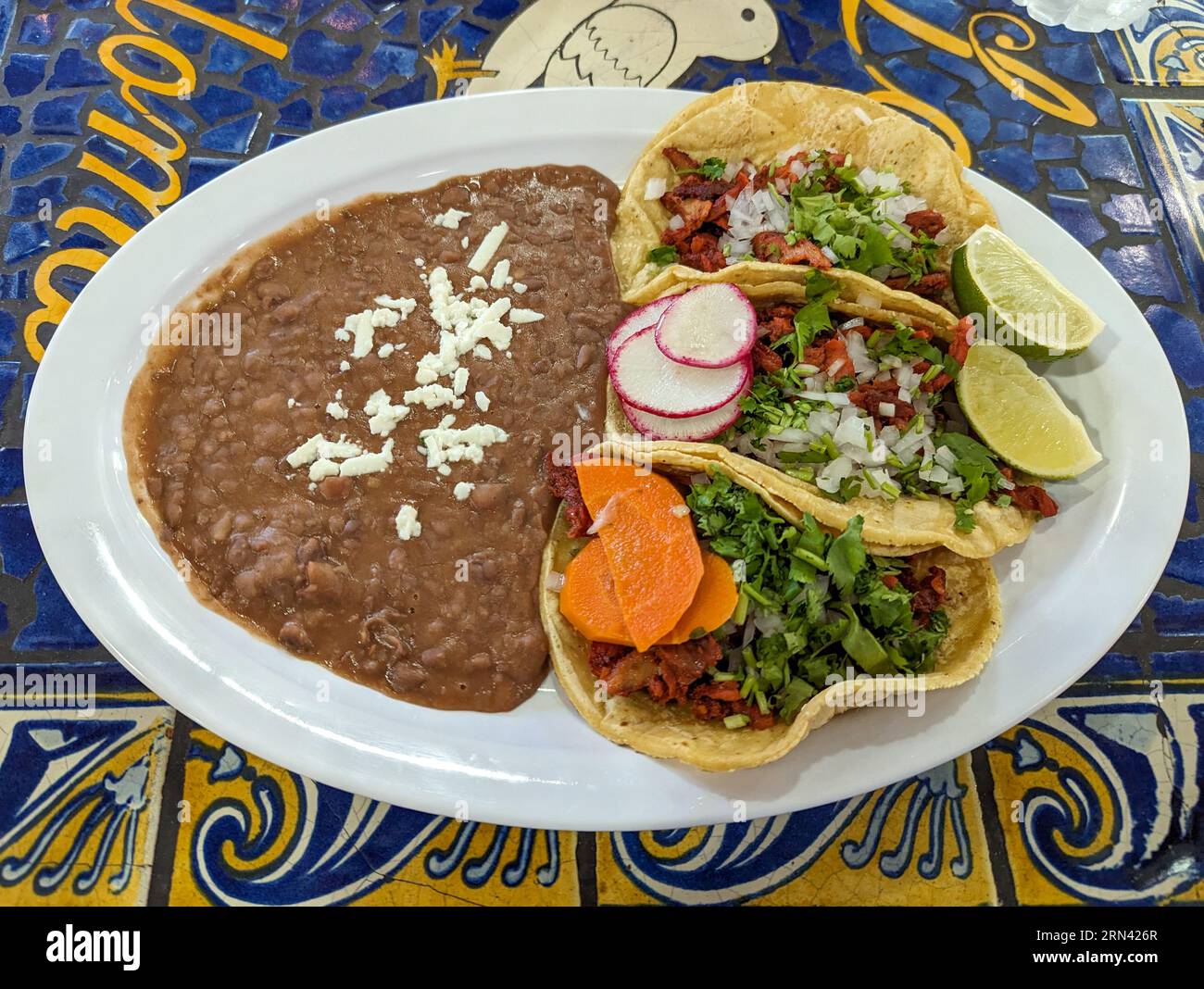 Ein Teller mit köstlichen Al Pastor Tacos und einer Seite mit gekühlten Bohnen. Stockfoto