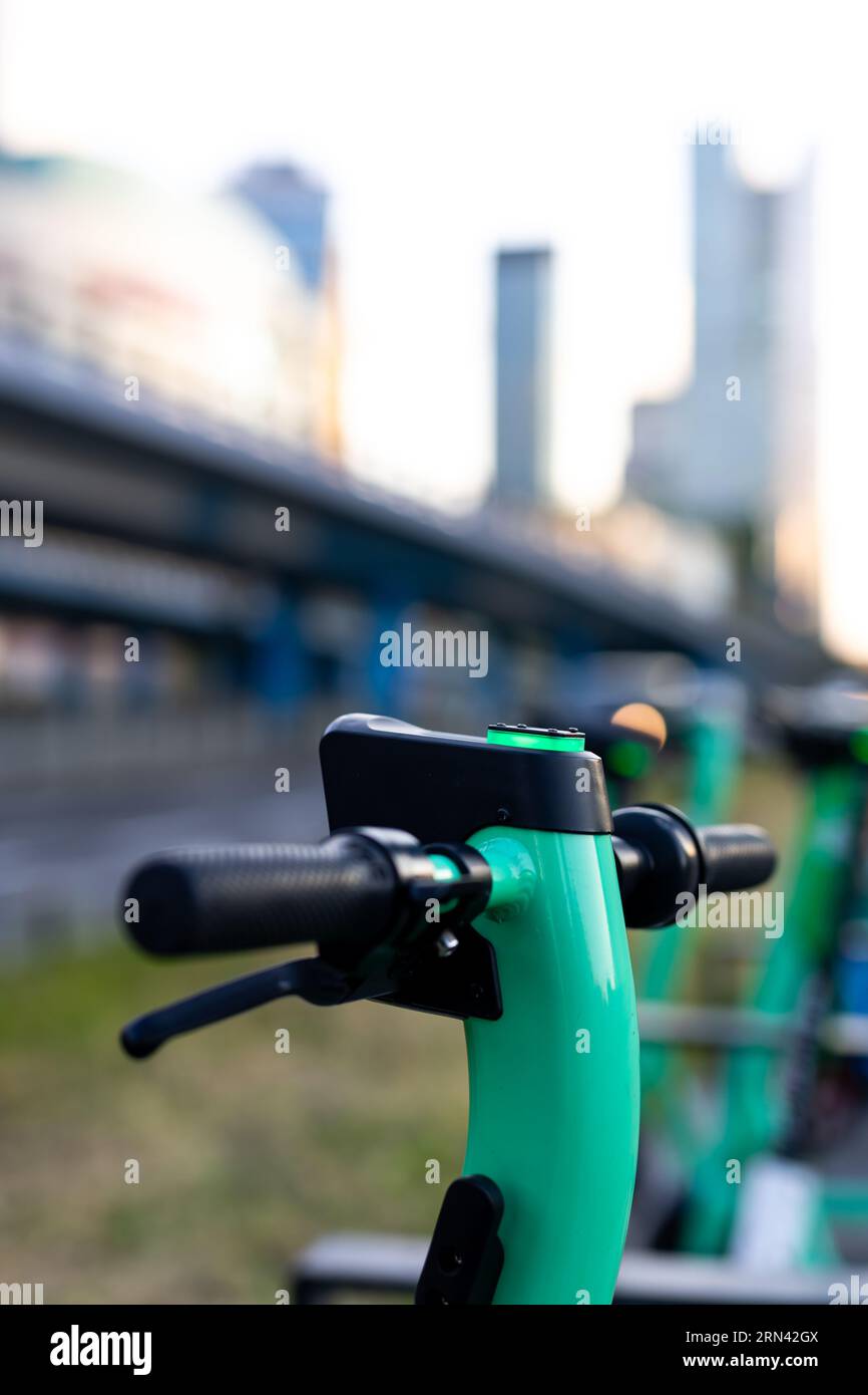 Nahaufnahme des Lenkers eines grünen Elektrorollers. Verschwommene Stadt im Hintergrund. Privatfahrzeuge für den Stadtverkehr können gemietet werden Stockfoto