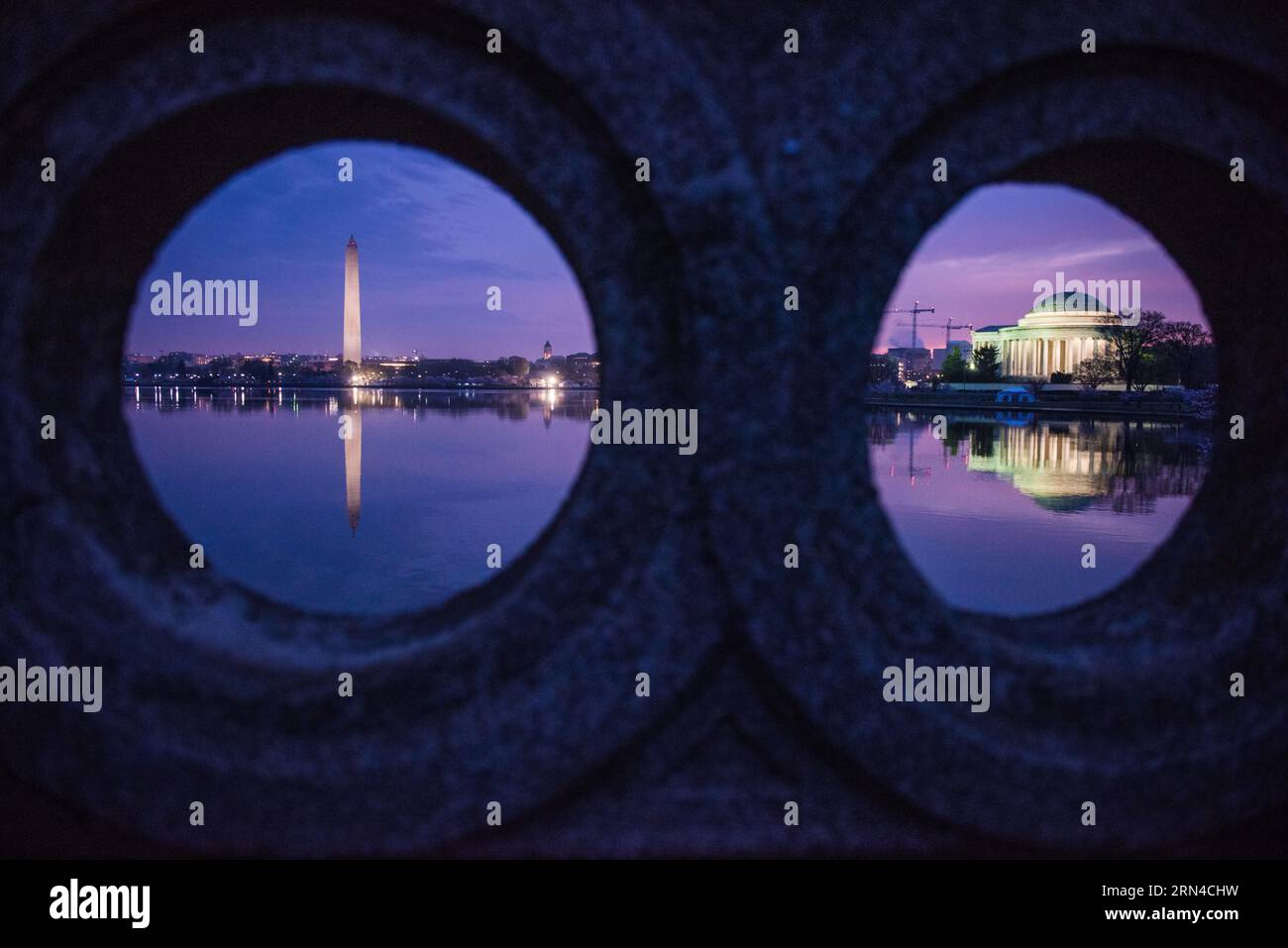 Washington Monument Jefferson Memorial Tidal Basin Washington DC // WASHINGTON, D.C., Vereinigte Staaten – Ein einzigartiger Blick auf das Washington Monument und das Jefferson Memorial, eingerahmt von den runden Portalen der Ohio Drive Bridge in der Vordämmerung. Die berühmten Wahrzeichen spiegeln sich in den stillen Gewässern des Tidal Basin wider und schaffen eine ruhige und symmetrische Komposition. Stockfoto