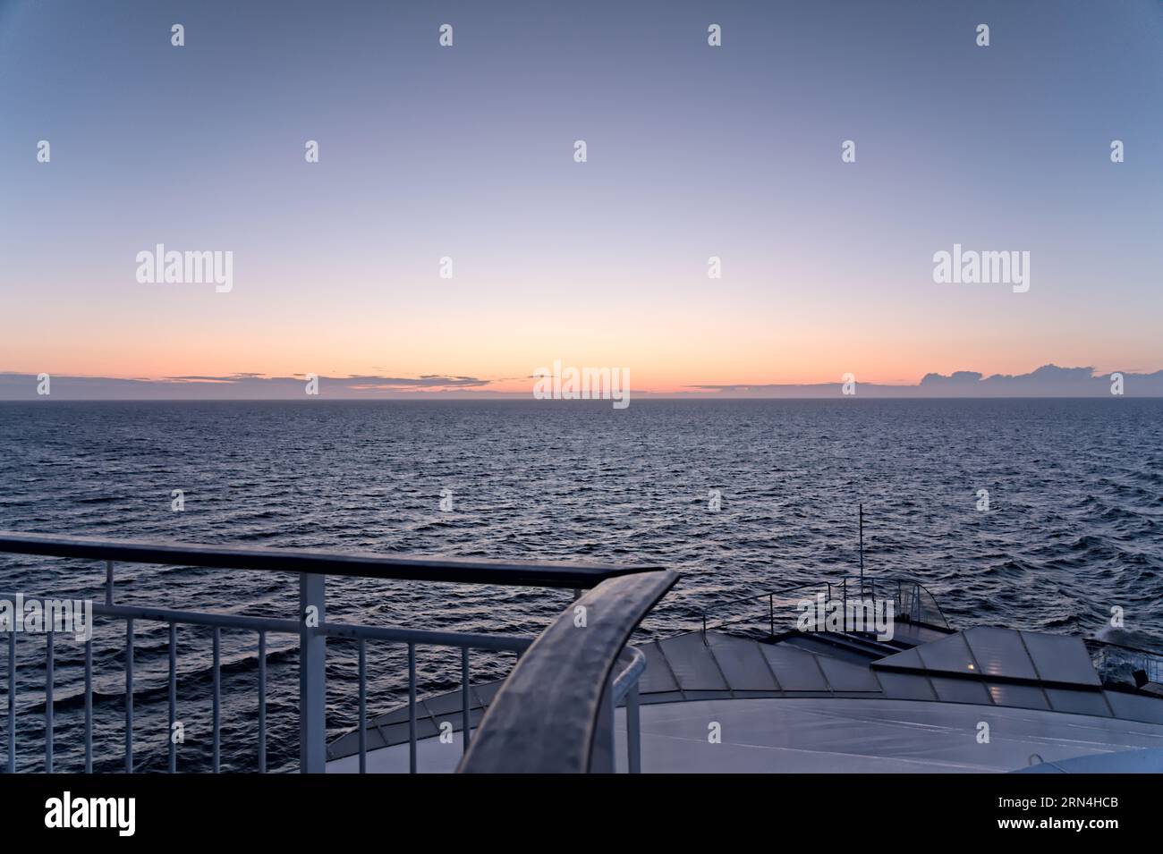 Blick auf das wellenförmige Meer und einen wunderschönen orange-blauen Abendhimmel auf dem Achterdeck des Kreuzfahrtschiffes. Konzept für den Sommerurlaub Stockfoto