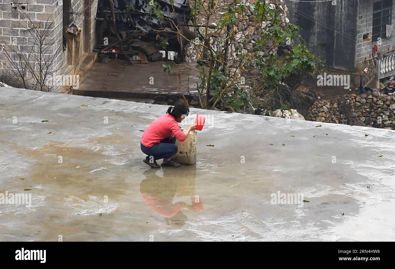 Lan Xiuxiang sammelt Regenwasser auf dem Dach ihres Hauses im Dorf Nongyong der Gemeinde Bansheng im Autonomen Kreis Dahua Yao, südwestchinesische autonome Region Guangxi Zhuang, 12. Februar 2015. Die Bansheng Township liegt im Zentrum der Karst-Landformen im Westen von Guangxi und leidet seit Ewigkeiten unter einem starken Wassermangel. Die Niederschläge sind daher ein Segen für die Menschen, die seit etwa 1.000 Jahren auf diesem Land leben und hauptsächlich der ethnischen Gruppe der Yao angehören. Um ihren täglichen Lebensbedürfnissen gerecht zu werden, sammeln die Einheimischen immer Regenwasser mit Eimern und Fässern jeder Größe sowie mit Dächern ihrer Häuser. In t Stockfoto