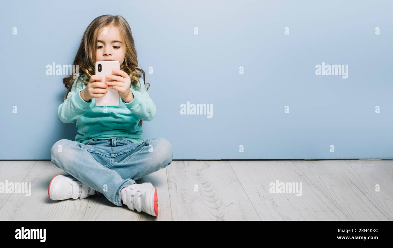 Porträt kleines Mädchen sitzt auf dem Hartholzboden und sieht aus wie ein Smartphone Stockfoto