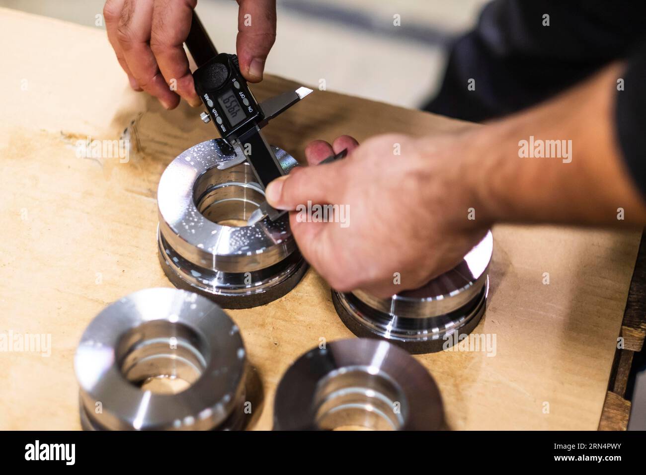 Ein Mann verwendet einen digitalen Messschieber, um die Größe einer Öffnung in einem Metallteil zu messen Stockfoto