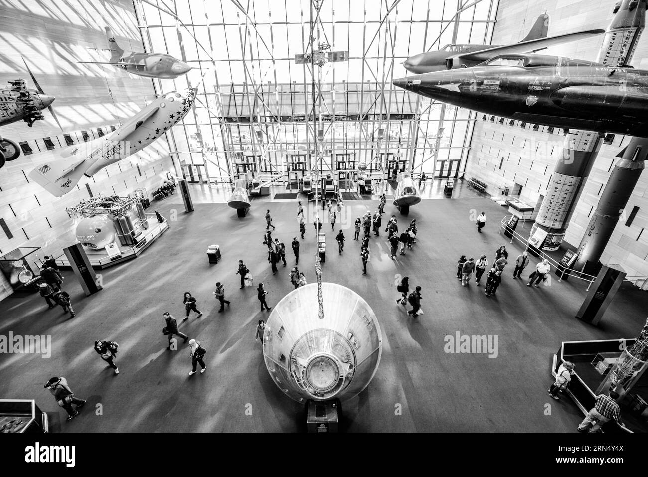 Air and Space Museum Interior, National Mall, Washington DC — Black and White Photo | WASHINGTON D.C., Vereinigte Staaten — ein erhöhter Schwarzweiß-Blick auf die Haupthalle des National Air and Space Museums zeigt Besucher, die unter Raumfahrzeugen und Raketenflugzeugen umherlaufen, darunter die Bell X-1, das erste Flugzeug, das die Schallmauer durchbrach, das 1947 von Chuck Yeager geflogen wurde. Kapseln und Raketen verfolgen die Geschichte der amerikanischen Raumfahrt von Mercury aus durch das Apollo-Programm. Stockfoto
