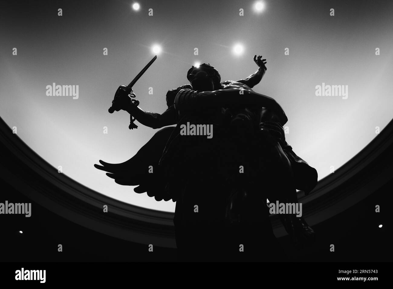 Geflügelte Siegesstatue. Schwarzweiß-Foto mit einem niedrigen Winkel der Statue vor einem hellen, neutralen Hintergrund. Stockfoto