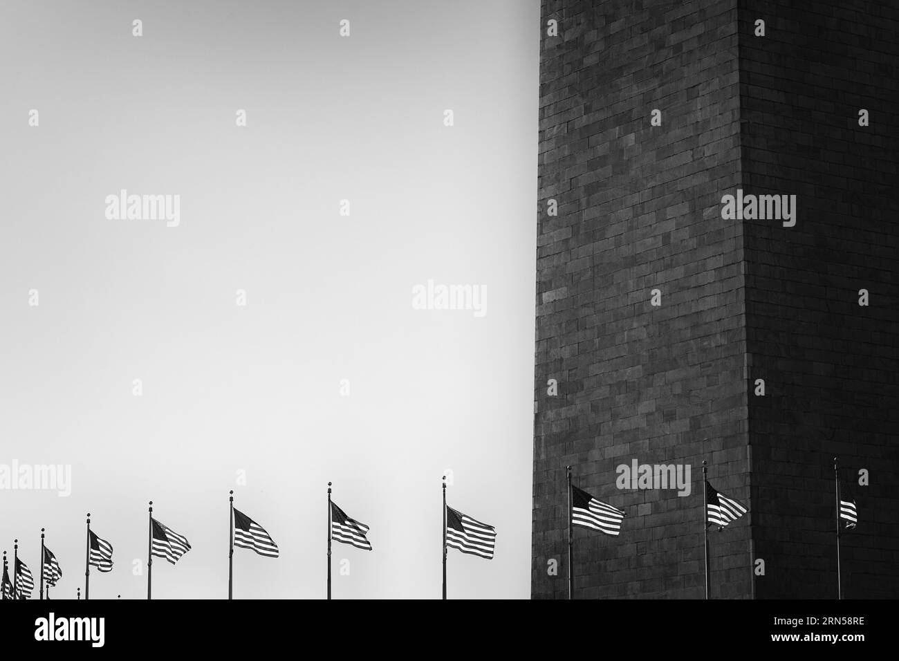 Washington Monument and Flags, Washington, D.C. Schwarzweißfoto, das die strukturierte Oberfläche des Obelisken und eine Reihe amerikanischer Flaggen vor hellem Himmel zeigt. Stockfoto