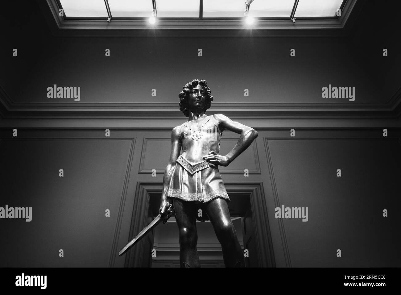 Statue mit Schwert. Schwarzweißfoto der Skulptur aus einem niedrigen Winkel, mit einem Oberlicht darüber. Stockfoto