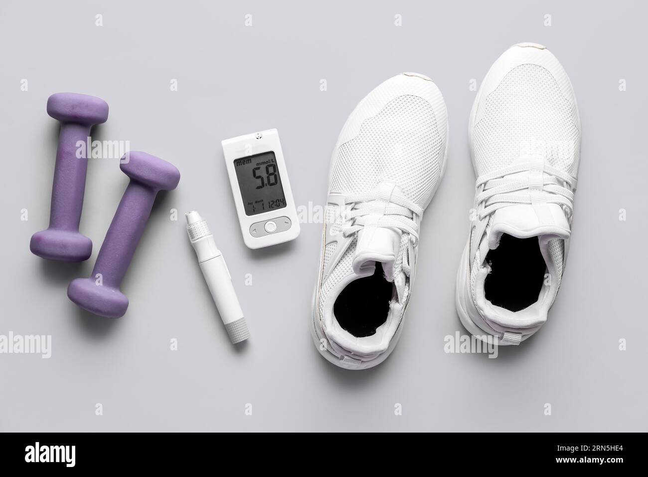 Glucometer, Turnschuhe, Lanzette und Kurzhanteln auf grauem Hintergrund. Diabetes-Konzept Stockfoto