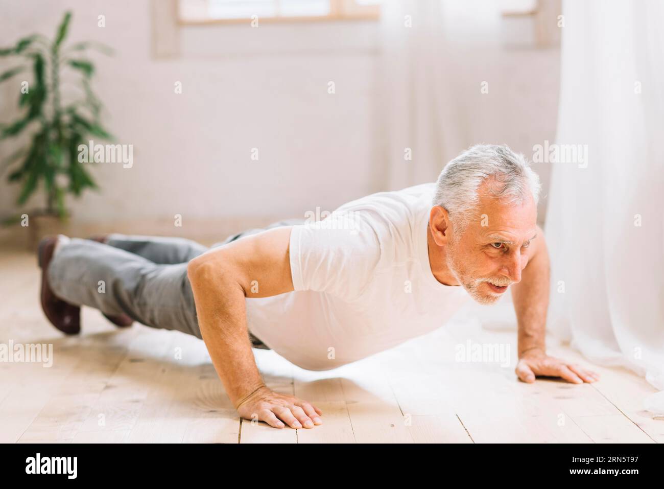 Älterer Mann, der eine Liegestützübung auf dem Hartholzboden machte Stockfoto