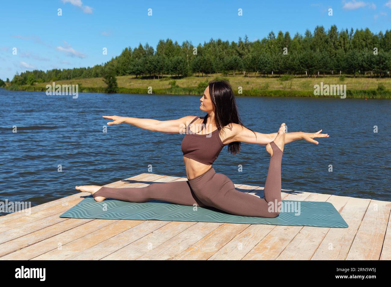 Eine Frau, die Yoga praktiziert, führt eine Variation der Hanumanasana-Übung durch, eine Längsspaltung, trainiert in separater Sportkleidung, während sie auf einer Woo sitzt Stockfoto