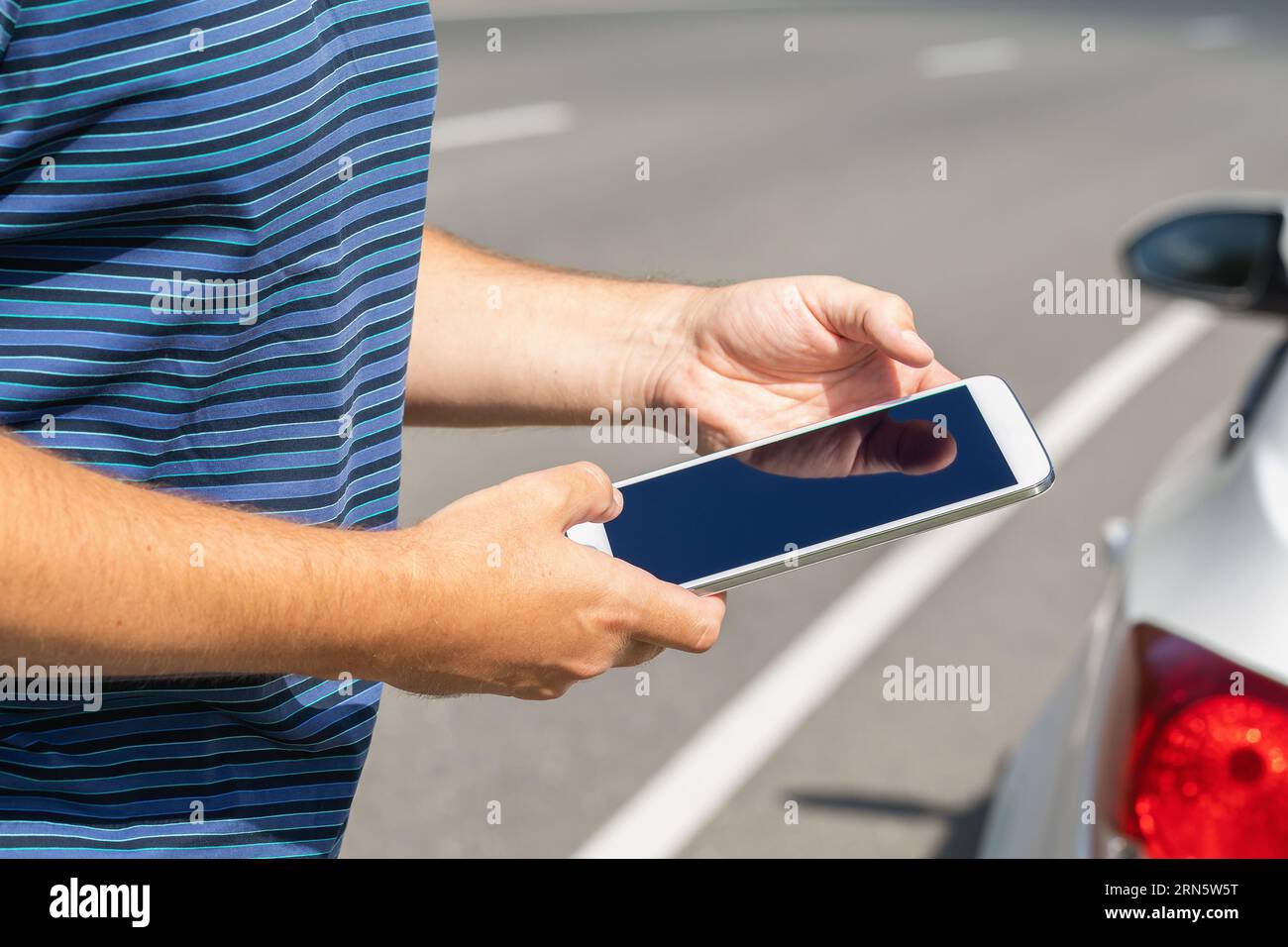 Ein Mann mit einem Tablet auf der Straße in der Nähe des Autos, ein Konzept zum Thema der Suche nach einer möglichen Fehlfunktion auf der Straße Stockfoto