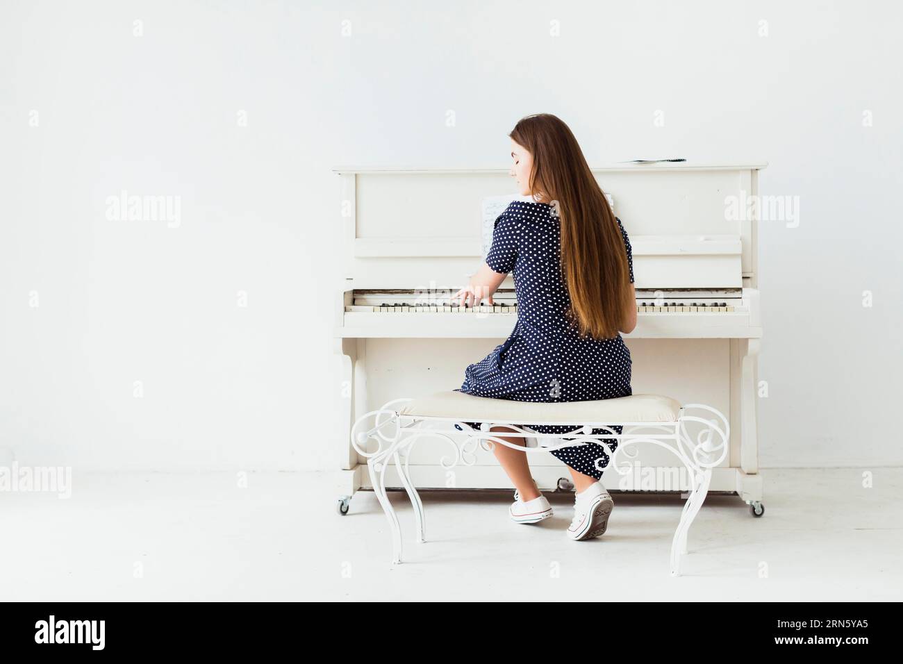 Rückansicht junge Frau mit langen Haaren, die Klavier gegen weiße Wand spielt Stockfoto