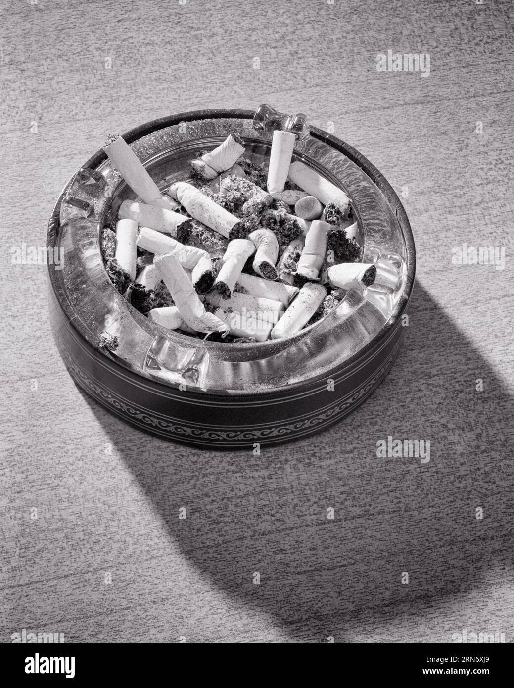 1960er Jahre RUNDE Aschenschale voll von Zigarettenkippen WERFEN Einen SCHATTEN - s10375 HAR001 HARS HINTERN EKLIGE GEWOHNHEIT SCHWARZ-WEISS ABHÄNGIGKEIT KRANKHEIT HAR001 GERUCH ALTMODISCH Stockfoto