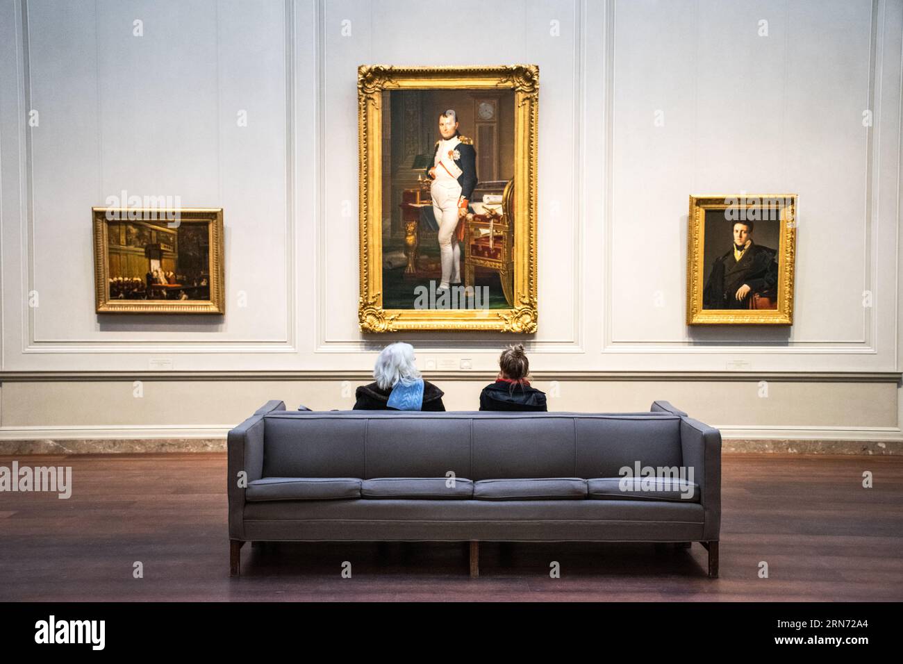 National Gallery of Art Napoleon Painting Washington DC // WASHINGTON DC — zwei Besucher sitzen auf einer Couch in der National Gallery of Art und bewundern Jacques-Louis Davids Meisterwerk „der Kaiser Napoleon in seiner Studie in den Tuilerien“ (1812). Das Gemälde, eine berühmte Darstellung von Napoleon Bonaparte, ist in der ständigen Sammlung des Museums ausgestellt und bietet Besuchern ein intimes Erlebnis dieses bedeutenden Kunstwerks der neoklassischen Kunst. Stockfoto