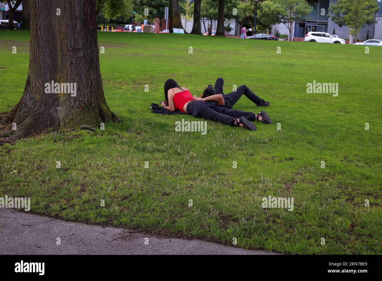 Im Tom McCall Waterfront Park im Zentrum von Portland, Oregon, ruhen sich Mann und Frau im Gras aus Stockfoto