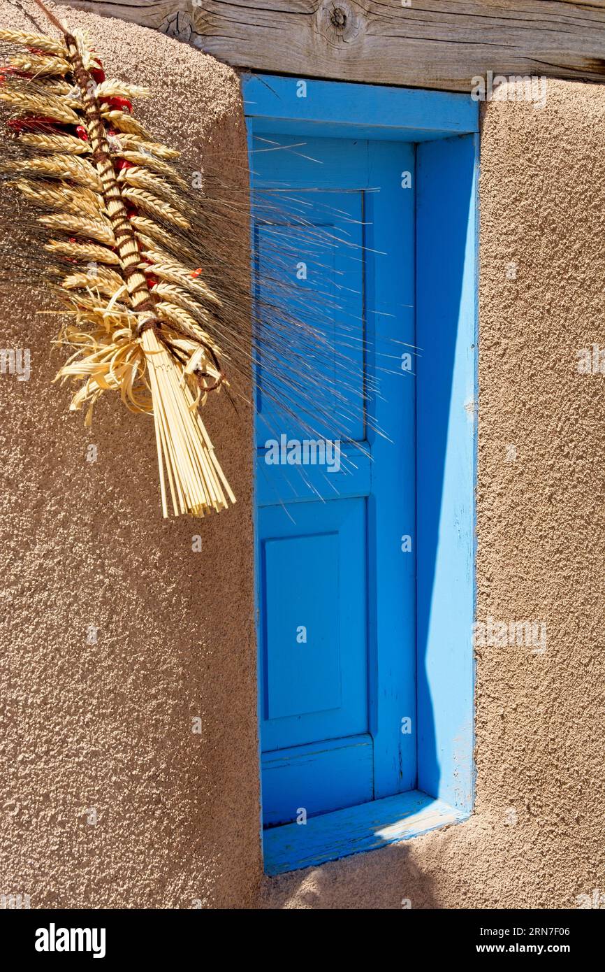Dekorative Weizenschale hängt am Holzsturz über einem blauen Fensterfenster in lehmziegeln am historischen Ranchos de Taos plaza in New Mexico Stockfoto