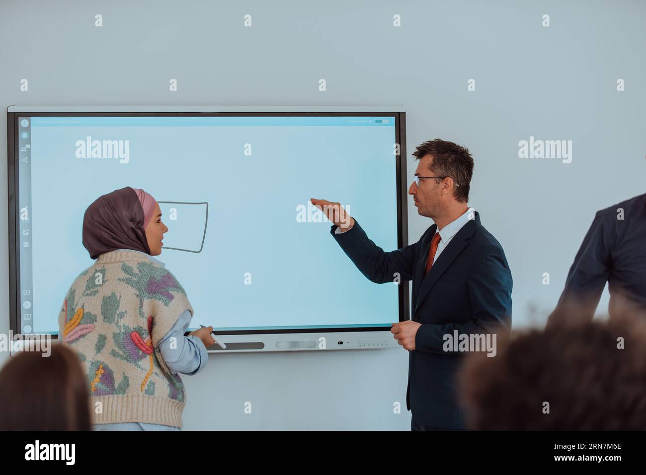 Ein modern gekleideter Professor vermittelt Studenten, die aufmerksam zuhören, und schafft eine dynamische Szene des Wissensaustauschs und fokussierten Lernens Stockfoto