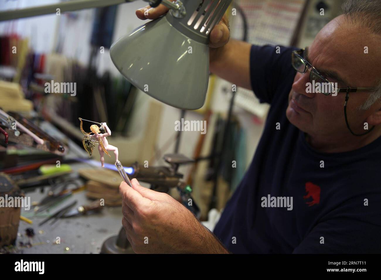 (150919)-- VENEDIG, 19. September 2015-- Lucio Bubacco schaut unter einer Lampe in den Glasengel, als er am 9. September 2015 in seinem Atelier in Murano in Venedig an seinem neuen Projekt Adam und Eva arbeitet. In Murano von Venedig, bekannt für seine Glaskunst, werden erfahrene Glashandwerker oft als Meister bezeichnet. Lucio Bubacco, der von vielen professionellen Glashandwerkern als echter Künstler angesehen wird, nennt sich jedoch nie Meister. Ich kümmere mich nicht um die Kommentare anderer Leute , sagte Bubacco, was mir wirklich wichtig ist, sind meine Beziehungen zu meinem Glas . In Murano setzen die Handwerker normalerweise Glasprodukte in den Raum Stockfoto