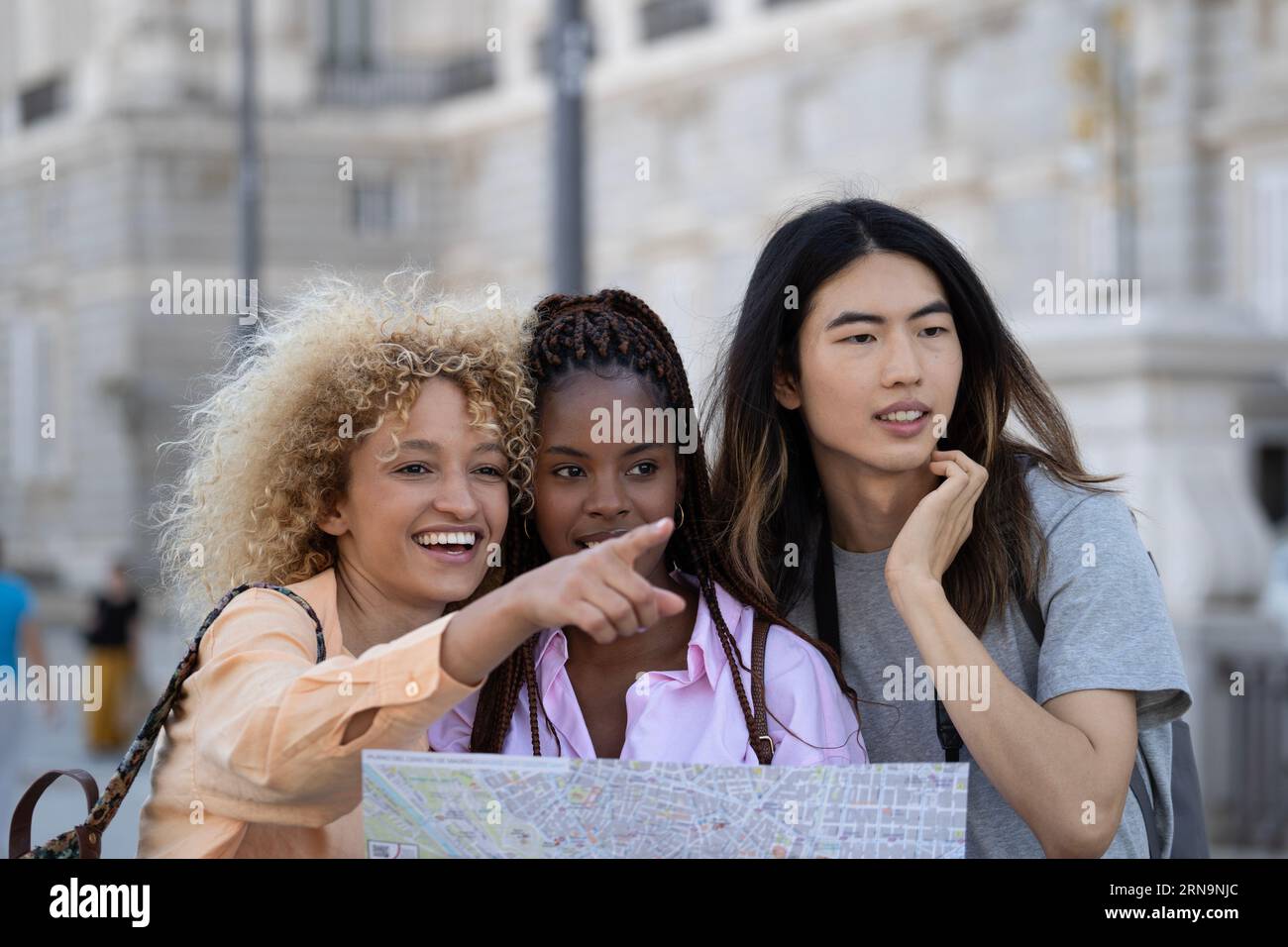 Gruppe junger, multiethnischer, lächelnder Touristen, die Madrid besuchen. Ein Mädchen hält eine Karte auf ihren Händen. Stockfoto