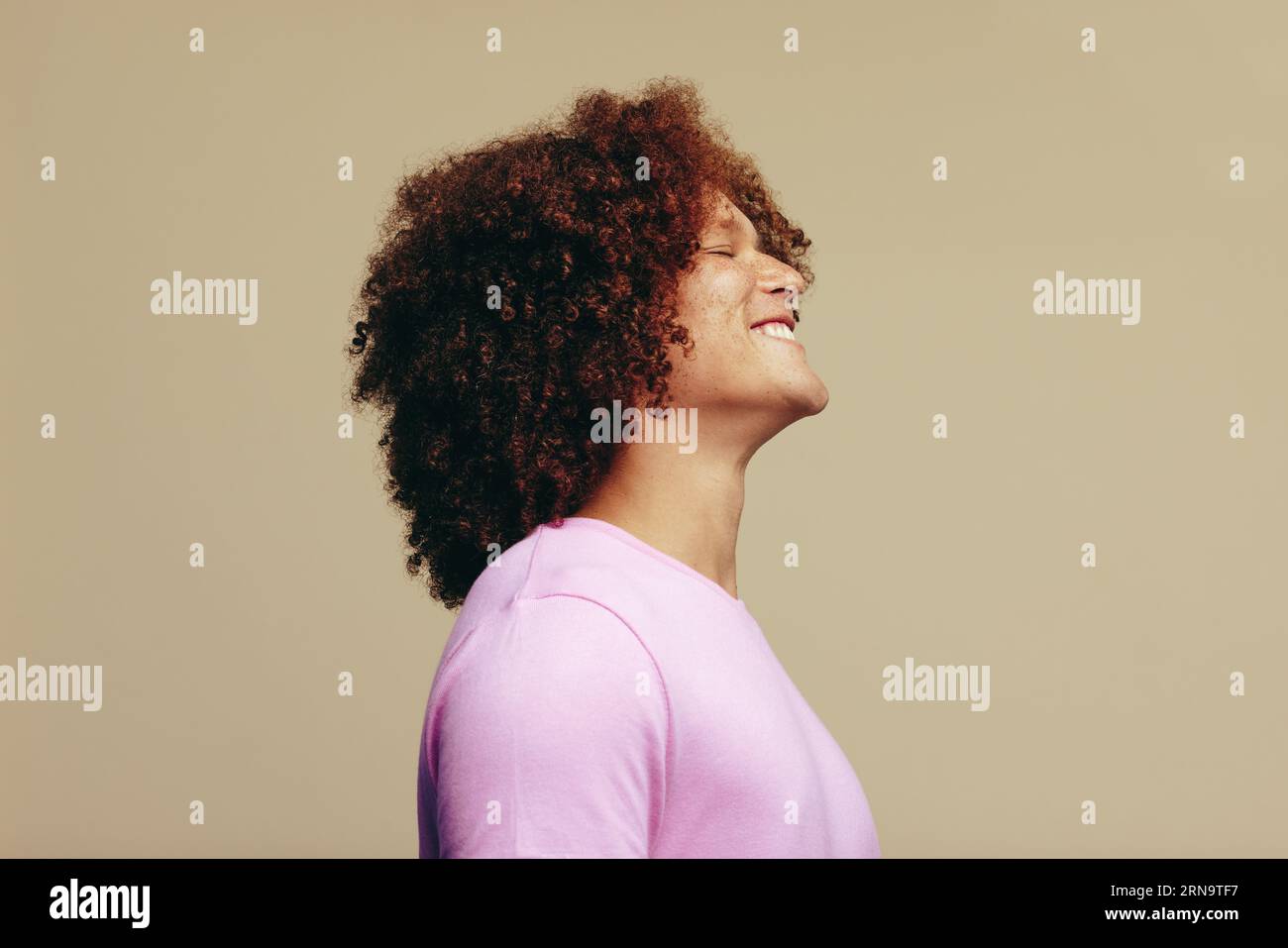 SideView eines jungen Mannes mit lockigem Ingwerhaar und ausgefranster Haut, der seine einzigartige Schönheit in einem Studio feiert. Gutaussehender Mann, der glücklich lächelt, während er ausdrückt Stockfoto