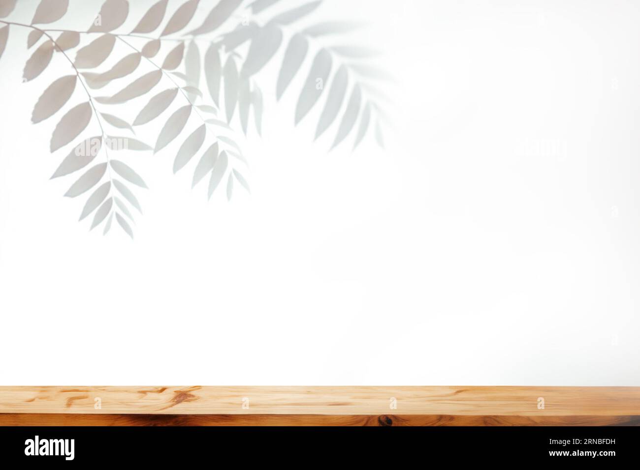 Holztisch und helle Wand mit verschwommenem Schatten aus Palmblättern Stockfoto