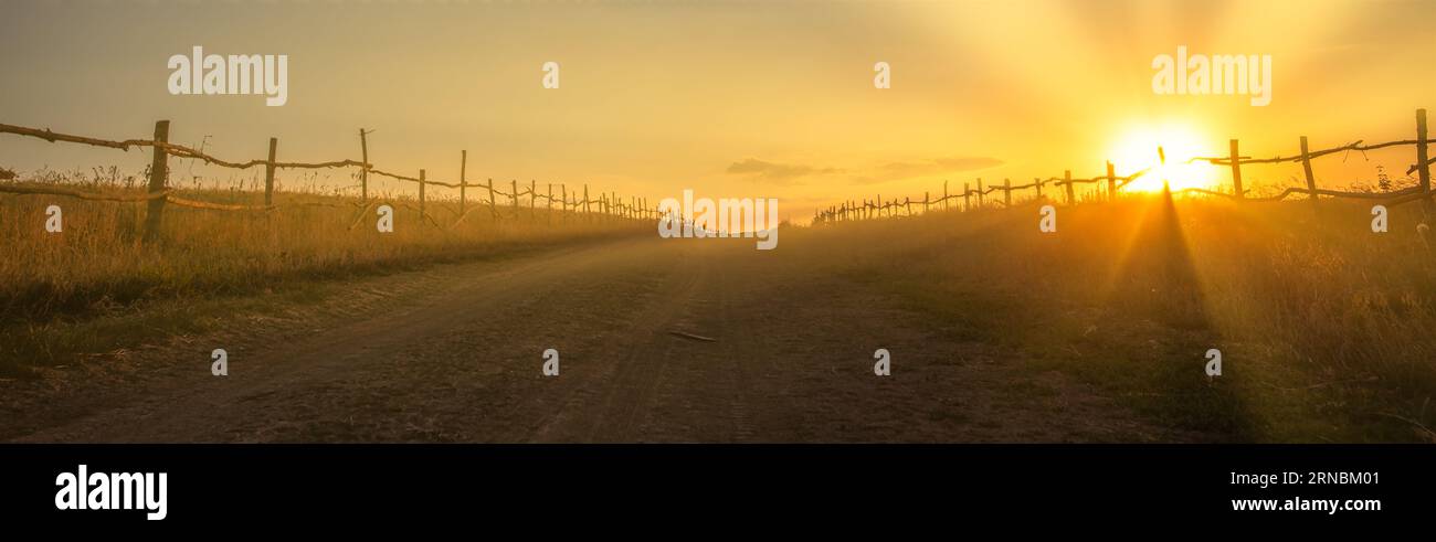 Der Charme von Sundown: Verwitterter Zaun und Country Road in Twilight Stockfoto