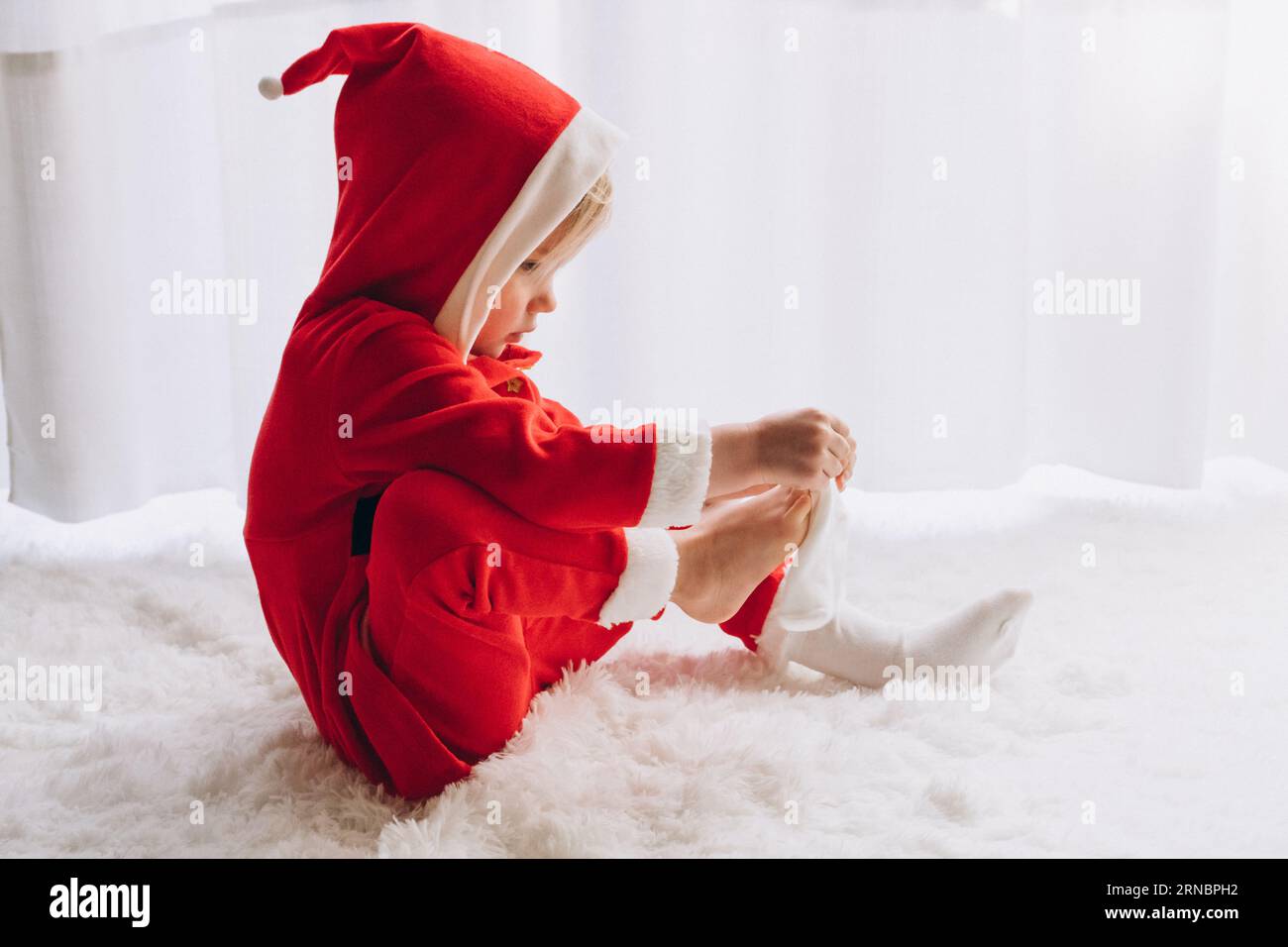 Das Kind sitzt im Weihnachtsmann und zieht Socken an Stockfoto