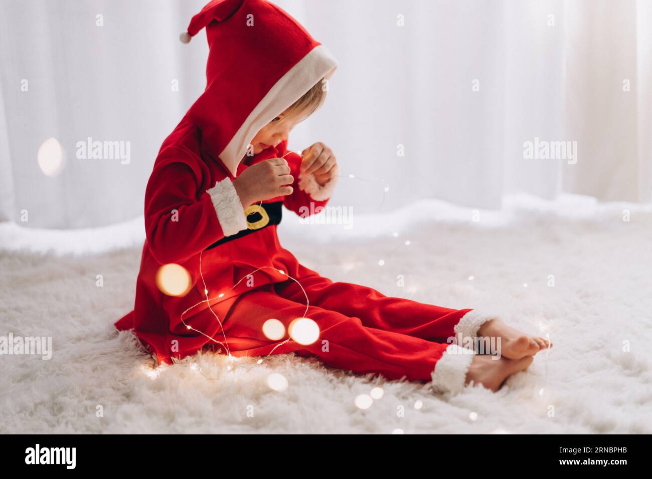 Ein Kind in einem Weihnachtsmann-Kostüm sitzt und schaut auf die Lichter Stockfoto