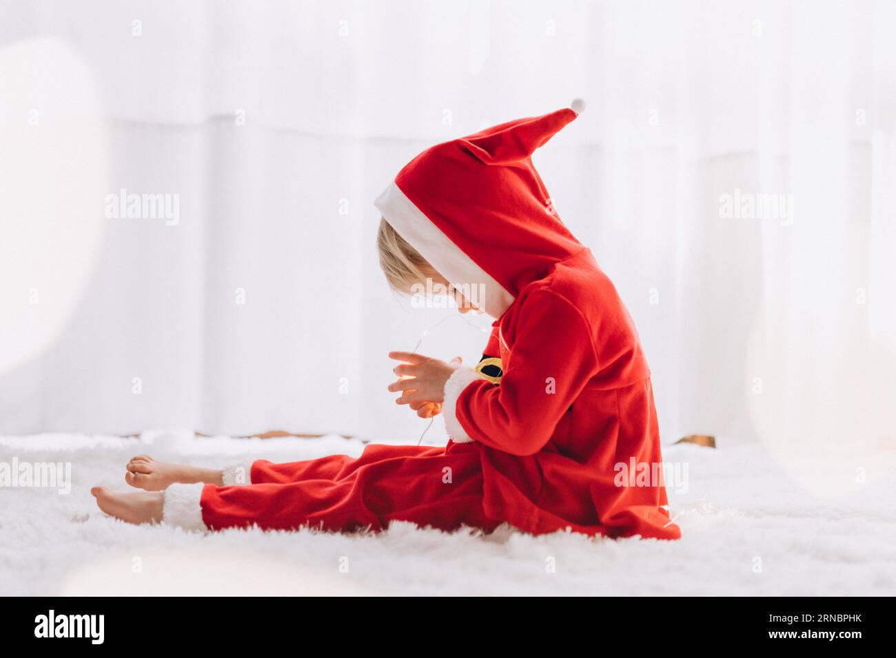 Ein Kind in einem Weihnachtsmann-Kostüm sitzt und schaut auf die Lichter Stockfoto