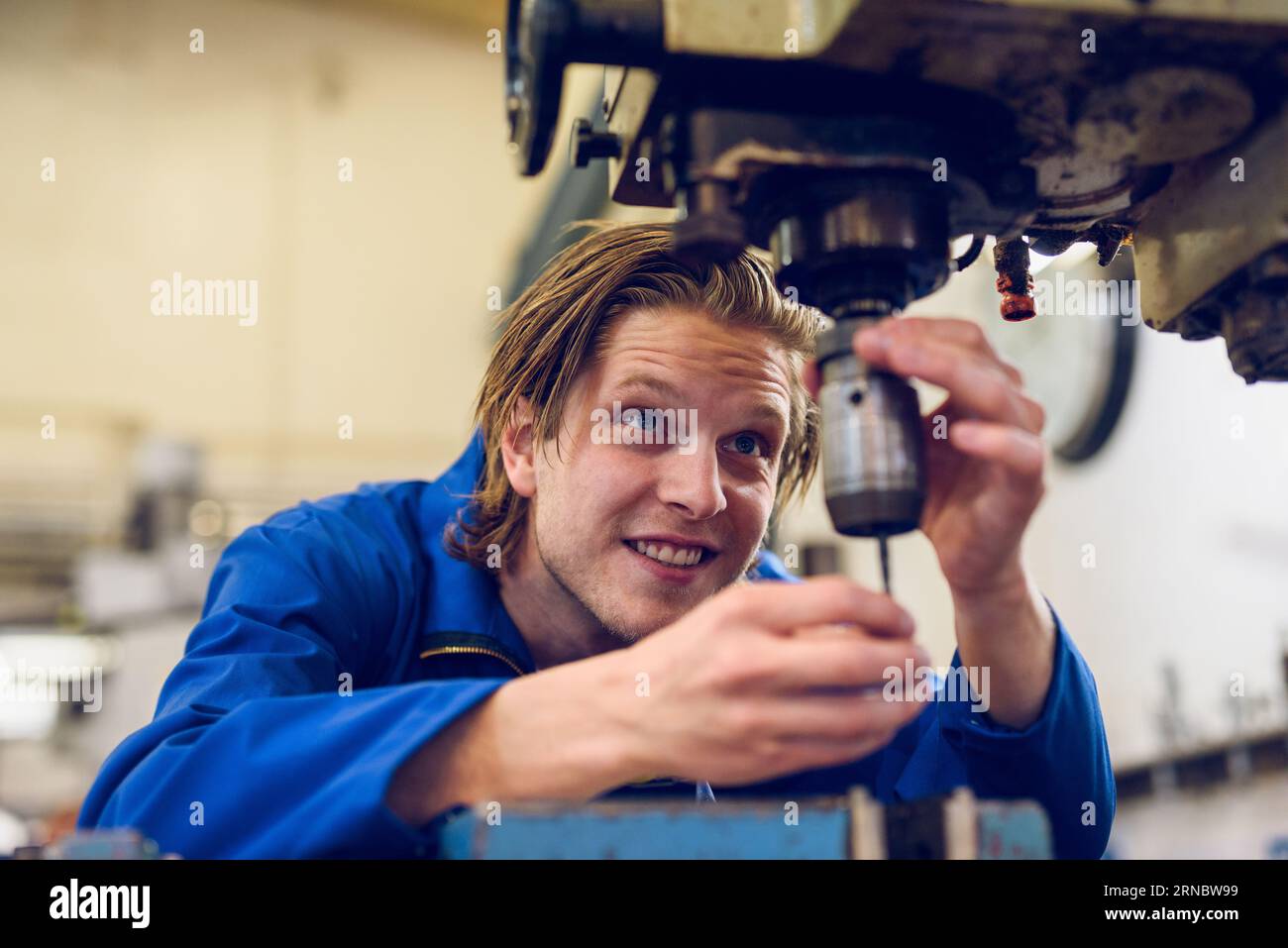 Glücklicher junger Mann, der an der Bohrmaschine steht und in der Fabrik repariert Stockfoto