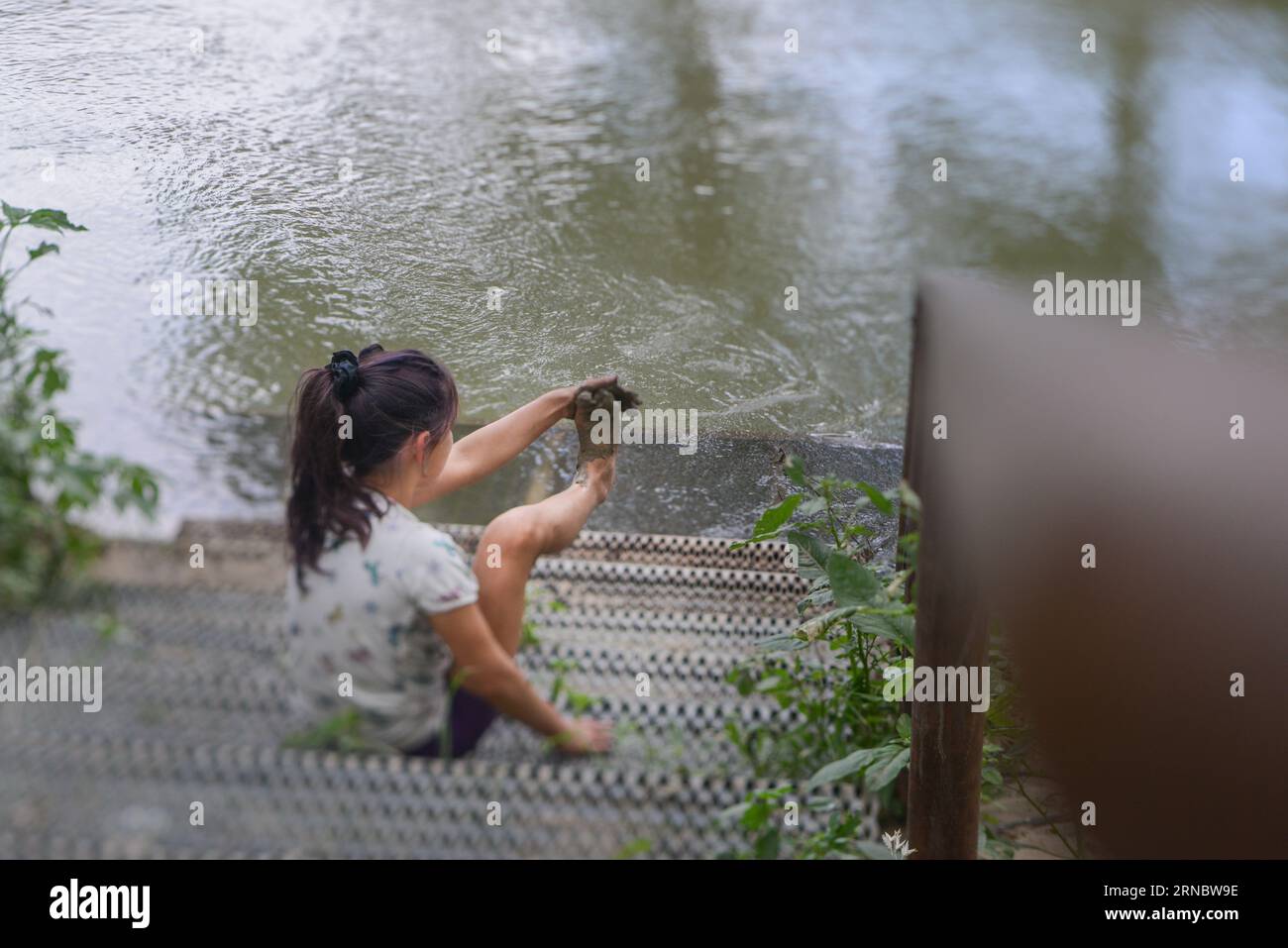 Mädchen spielt in Schlamm neben Wasser Stockfoto